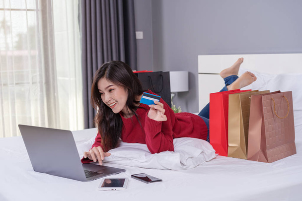 happy woman using laptop computer for online shopping with credit card on a bed - Foto, Bild