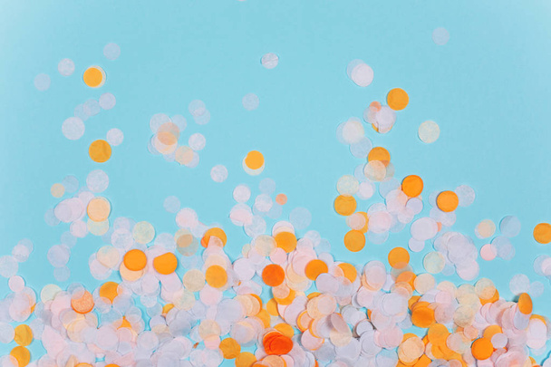 Orange and yellow colorful festive confetti on blue. Flat lay style. - Foto, imagen