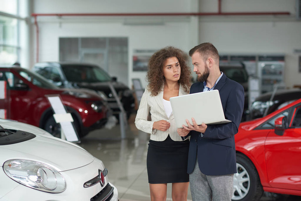 Manager of car dealership showing automobile to woman. - Foto, afbeelding