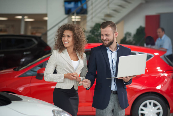 Happy woman choosing car with manager of car dealership. - Foto, afbeelding