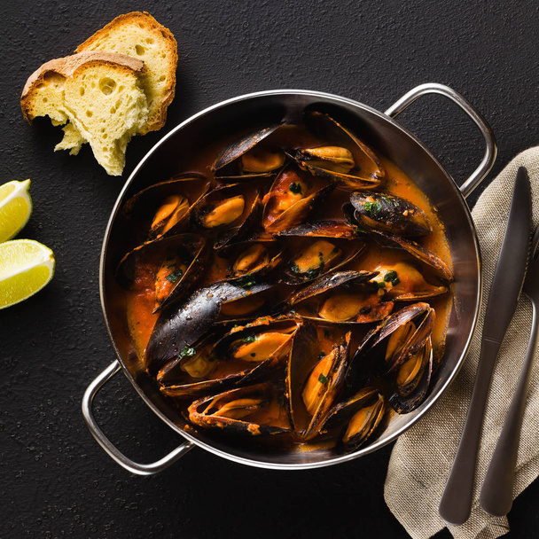 freshly cooked mussels in a frying pan in tomato sauce. pepata di cozze or mussels marinara. classic dish of mediterranean italian cuisine. on black background - Photo, Image