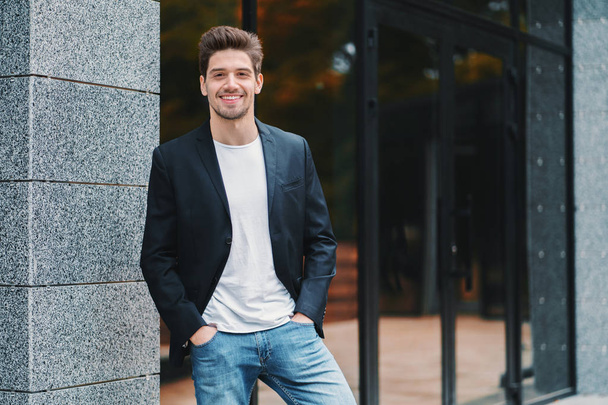 Portrait of young successful confident businessman in the city on office building background. Man in business suit looking to camera and smiling. Portraiture of handsome guy. - Fotografie, Obrázek