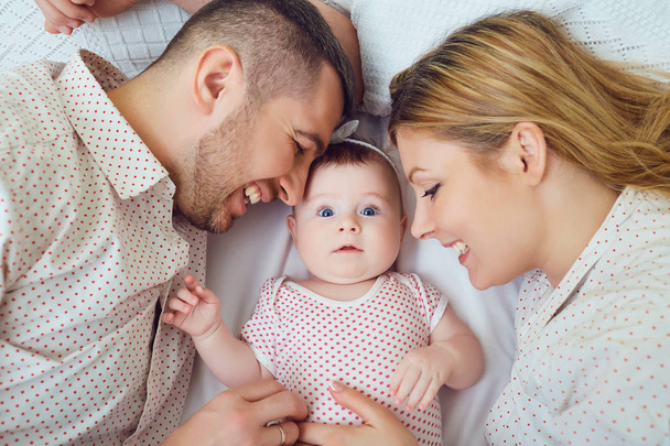 A happy family plays with a toddler on a bed in a room indoors. - Foto, Bild