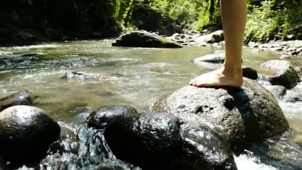 Jonge vrouw in een zwembroek zit op een steen en spetterend water in een koude rivier berg - Video