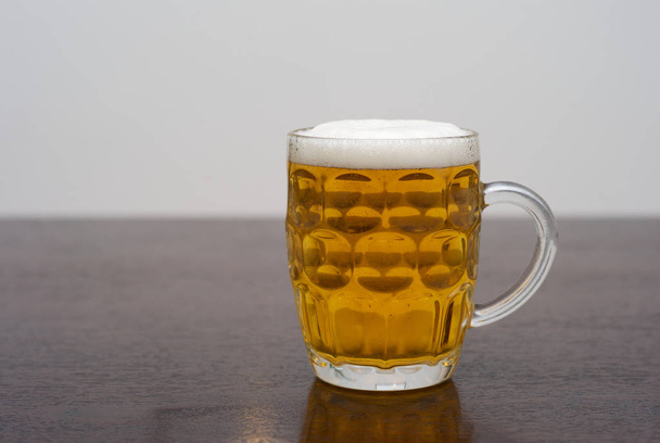 Bir bardak bira bira koyu ahşap bir masa üzerinde bir çukurlu Pint cam - Fotoğraf, Görsel