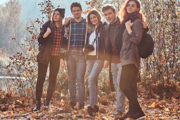 Группа молодых друзей обнимаются и смотрят в камеру в красивом осеннем лесу
. - Фото, изображение