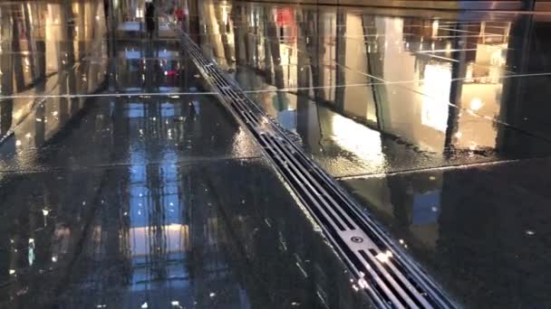 Granite Street ostoskeskuksen ulkopuolella Lontoossa sateisena päivänä. Ihmiset kävelevät ohi, märkä granit näyttää heijastaa kauppoja ostoskeskuksessa
 - Materiaali, video