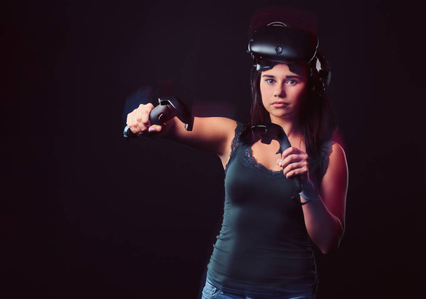 Красивая молодая женщина носит гарнитуру виртуальной реальности и держит джойстики, позируя ar камеры
. - Фото, изображение