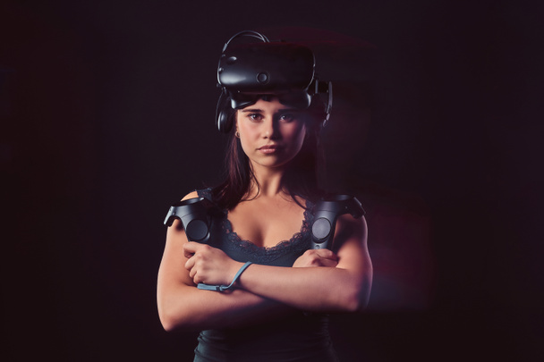 Portrait d'une jeune femme portant des lunettes de réalité virtuelle et tenant des joysticks, posant avec les bras croisés, regardant la caméra
. - Photo, image