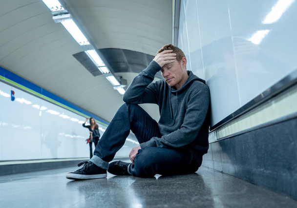 Miserable jobless young man crying Drug addict Homeless in depression stress sitting on ground street subway tunnel looking desperate leaning on wall alone in Mental disorder Emotional pain Sadness. - 写真・画像