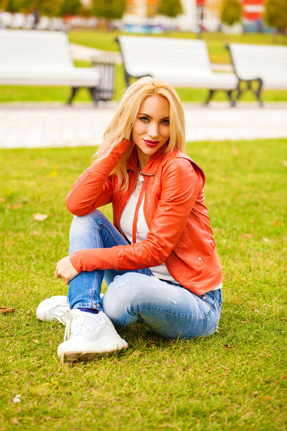 Young blonde woman in blue jeans in autumn park - Fotoğraf, Görsel