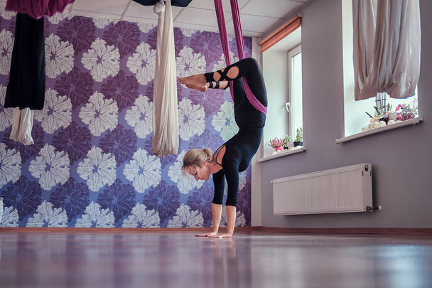 Молода жінка практикує повітряну йогу в фіолетовому гамаку в фітнес-клубі
. - Фото, зображення