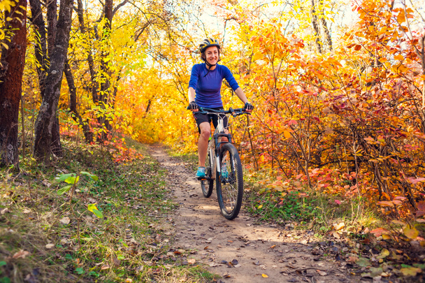 Biking in the forest. Girl rides a bike on a forest trail. Woman riding her bike in the park. Bicycle touring. Travel to scenic places. Autumn trees. - Фото, изображение