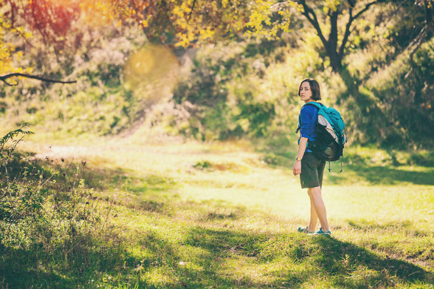 Een vrouw met een rugzak wandelingen door de herfst bos. Girl in het najaar park. Alleen reizen in schilderachtige plekjes. Een slanke vrouw loopt langs een bergpad. - Foto, afbeelding