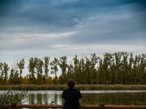 A person in a viewpoint with a wooden railing contemplating a river in autumn - Foto, Bild