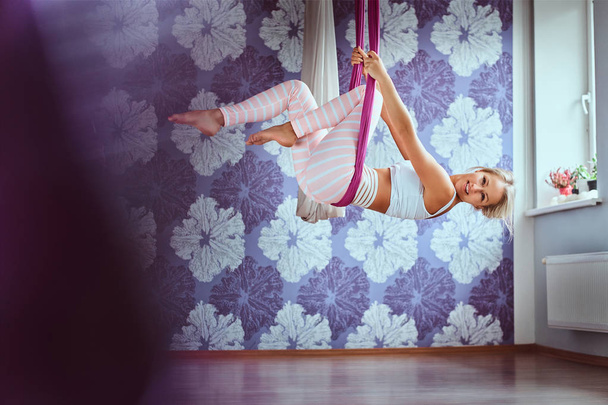 Young woman doing aerial yoga practice in purple hammock in fitness club. - Fotoğraf, Görsel