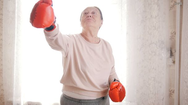 eine alte Seniorin, die in roten Handschuhen boxt und lächelt - Foto, Bild