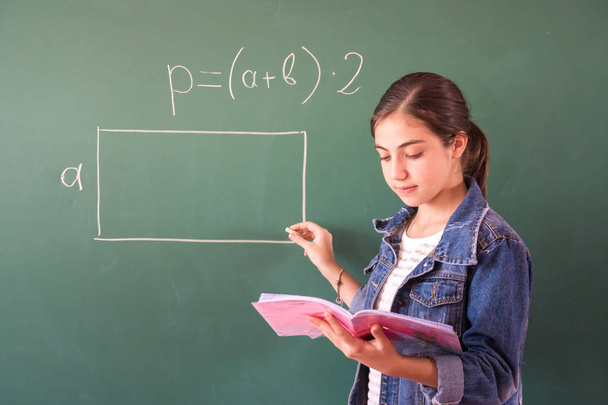 μαθήτρια με κιμωλία σε μαυροπίνακα λύνει ένα πρόβλημα μαθηματικών. - Φωτογραφία, εικόνα