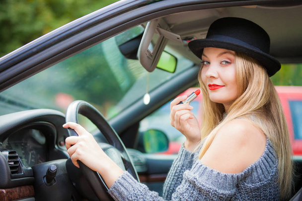 Молода приваблива жінка, дивлячись у дзеркало заднього виду, малює губи, використовуючи макіяж під час керування автомобілем
. - Фото, зображення