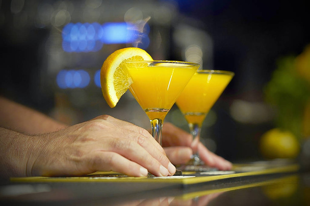 El barman le da un cóctel al cliente del bar del hotel. Cóctel fresco con naranja. Bebida alcohólica no alcohólica en el mostrador del bar del club nocturno. Copa de cóctel naranja
. - Foto, Imagen