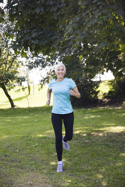 Front view of senior woman jogging through park - Photo, Image
