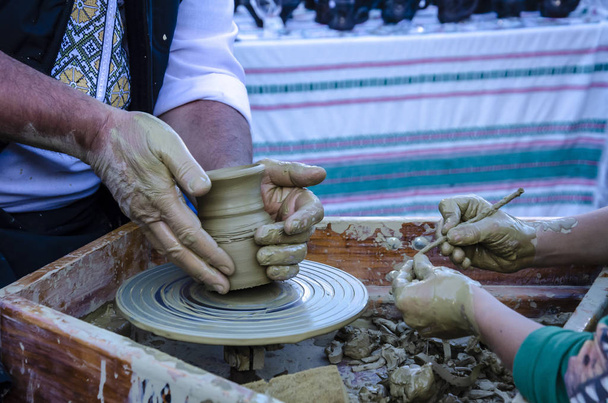 Las manos del alfarero trabajan y forman la arcilla para hacer una jarra pequeña y las manos de un niño
 - Foto, Imagen