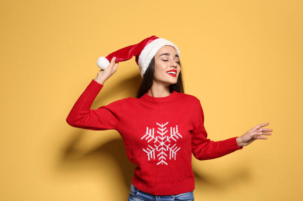 Young woman in Christmas sweater and hat on color background - Фото, зображення