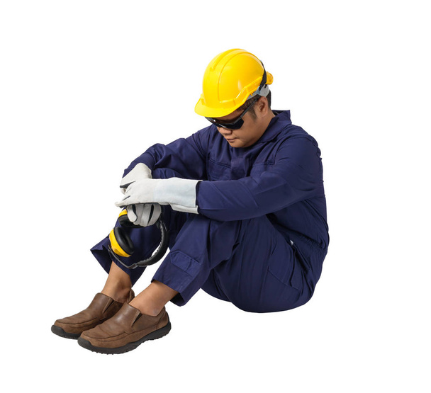 εργαζόμενος σε μηχανικό ολόσωμη φόρμα με κράνος, ωτοασπίδες, προστατευτικά γάντια και προστατευτικά δίοπτρα ασφάλειας κάθεται απομονώνονται σε λευκό φόντο διαδρομή αποκοπής - Φωτογραφία, εικόνα