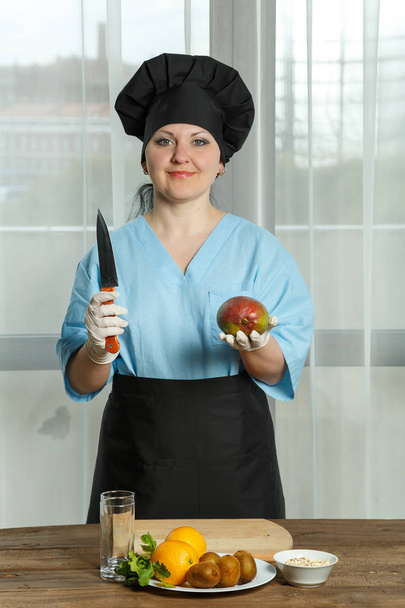 the woman the cook holds in one hand a fruit of mango and in other hand a knife. vertical image. - Foto, imagen