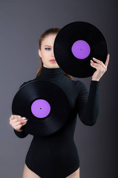 The girl is holding a vinyl disc in her hands, covering half the face. Studio shot on a gray background - Fotografie, Obrázek