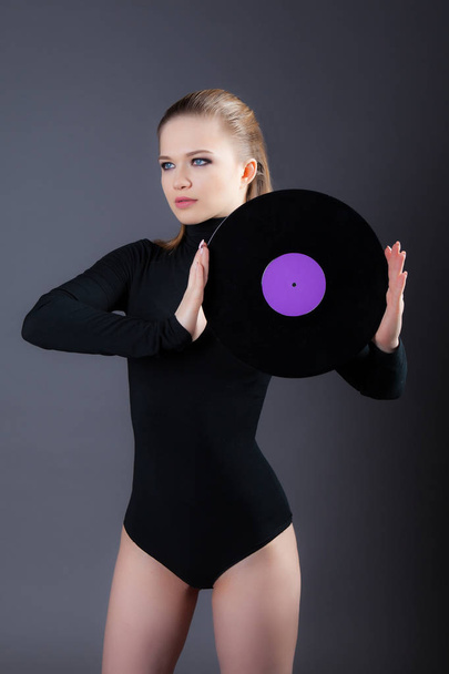 A beautiful girl is holding a vinyl disk. Studio photography on a gray background - Фото, изображение