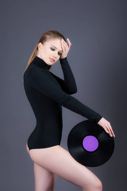 A beautiful girl is holding a vinyl disk. Studio photography on a gray background - Foto, imagen