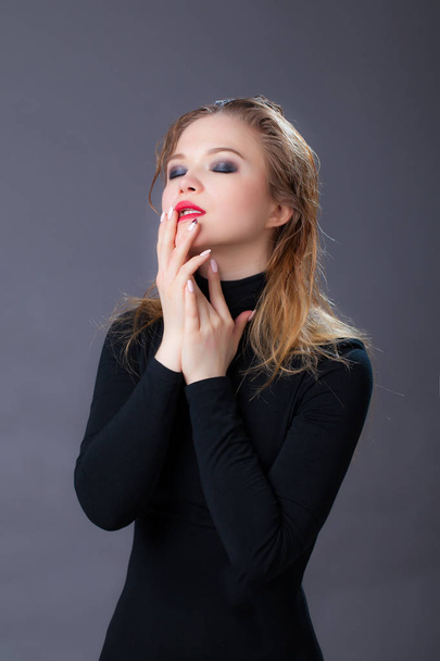 Portrait of a girl in black clothes, wet hair, holding hands on her face, eyes closed. Studio shot, against a gray background - Foto, afbeelding