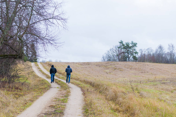 Dos hombres caminando por el camino rural en otoño. Clima nublado casi todos los días. Pero el aire fresco es sabroso y es un puro placer dar un pequeño paseo por los alrededores del país.
. - Foto, Imagen