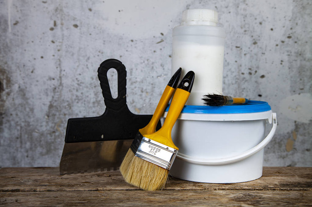  Farbdose und Pinsel auf dem Tisch. Gegenstände für die Renovierung zu Hause oder im Büro vor einer grauen Wand. - Foto, Bild