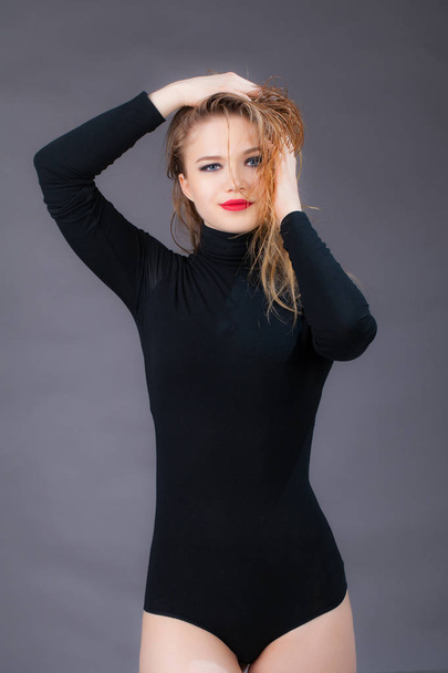Portrait of a girl in black clothes, holding her hands wet hair. Studio shot, on a gray background - Foto, immagini