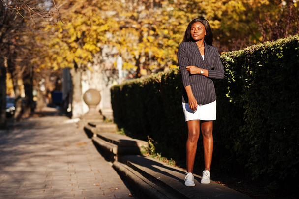 Erfolg stylische afrikanisch-amerikanische Frau in Jacke und Rock posierte an einem sonnigen Herbsttag auf der Straße. - Foto, Bild