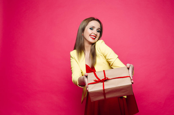 Beautiful happy woman in fashionable cat-eye glasses in bright dress holding Christmas present. - Foto, Bild