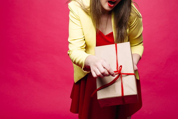 Beautiful happy woman in fashionable cat-eye glasses in bright dress holding Christmas present. - Foto, Imagen