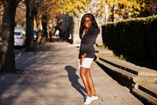Success stylish african american woman in jacket and skirt posed on sunny autumn day at street. - Foto, imagen