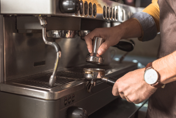 bijgesneden schot van barista koffie in houder aangedrongen koffiezetapparaat - Foto, afbeelding