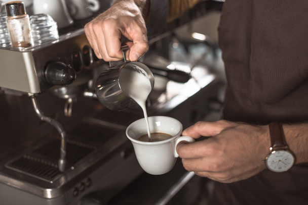 tiro cortado de barista derramando leite em café enquanto o prepara no restaurante
 - Foto, Imagem