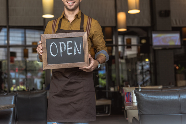 обрезанный снимок счастливого официанта держащего доску с открытой надписью в кафе
 - Фото, изображение