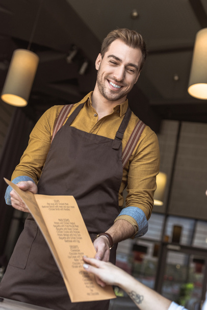 przycięte strzał uśmiechnięty kelner Wyświetlono listę menu do klienta w kawiarni - Zdjęcie, obraz