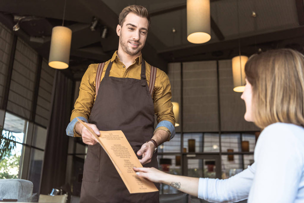 bel giovane cameriere che mostra la lista dei menu al cliente femminile nel caffè
 - Foto, immagini