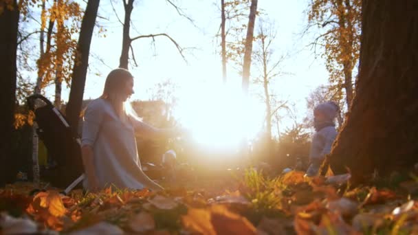 Młoda matka w sukni z jej małe dziecko grając w jesienny park. Piękne światło słoneczne - Materiał filmowy, wideo