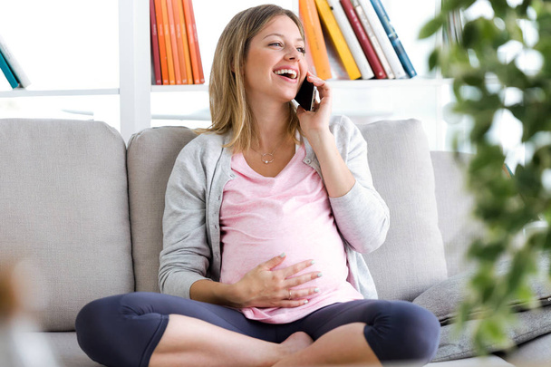 Shot of beautiful young pregnant woman talking with her smartphone on the sofa at home - Фото, зображення