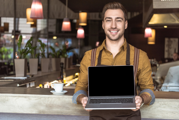 felice giovane cameriere che tiene il computer portatile con schermo vuoto in caffè
 - Foto, immagini