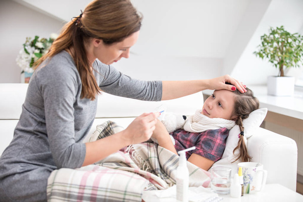 mother sits at the bedside of the sick daughter  and measures the temperature - Foto, Bild