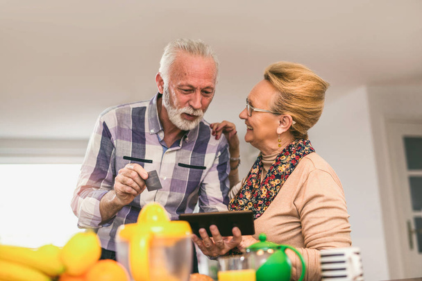 Idősebb pár segítségével digitális tábla és a hitelkártya-otthon a konyhában online vásárlás - Fotó, kép